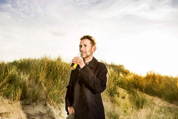 Smiling woman drinking a beer in dunes - obrazy, fototapety, plakaty