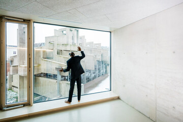 Back view of barefoot businessman with Virtual Reality Glasses standing on window sill looking out...