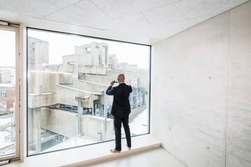 Back view of barefoot businessman standing on window sill taking picture with smartphone