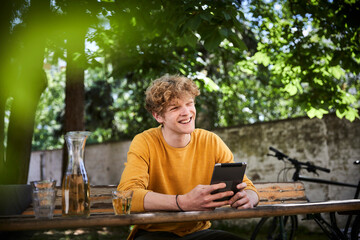 Portrait of young man sitting at beer table in garden with digital tablet
