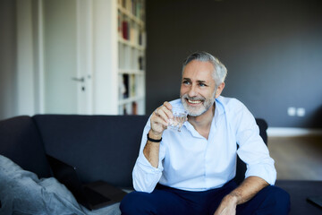 Smiling mature man drinking glass of water on the sofa at home