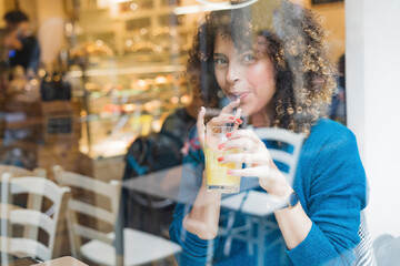 Portrait of woman drinking a smoothie behind windowpane in a cafe