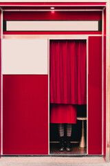 Woman wearing red coat and boots standing behind curtain in a photo booth