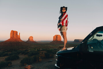 USA, Utah, Monument Valley, Woman with United States of America flag enjoying the sunset in...