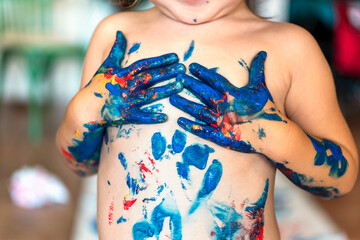 Toddler girl playing with finger paint making imprints on her chest