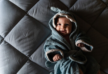 Portrait of happy baby girl lying on bed wrapped with shark shaped towel after bath