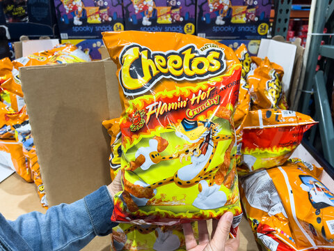 Shopper holding a Bag of Cheetos Flamin' hot brand cheese corn puffs snacks for sale at a local Costco warehouse  shelf