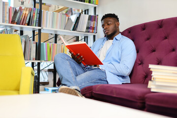 Young man, sitting, studying a book in a modern library, gaining knowledge for academic success.