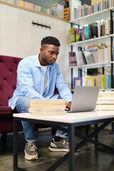 Obraz premium Young African businessman working on a laptop in a modern office, showcasing confidence and digital success.