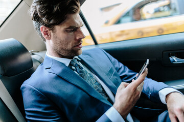 Businessman sitting in taxi, using smart phone