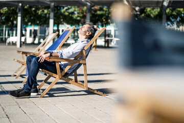 Mature man relaxing in deckchair on a square in the city