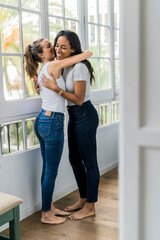 Two happy girlfriends hugging at the window at home