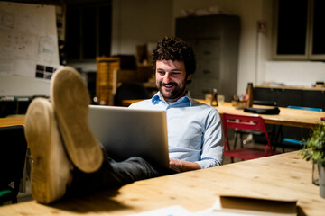 Businessman using laptop in office with feet on desk