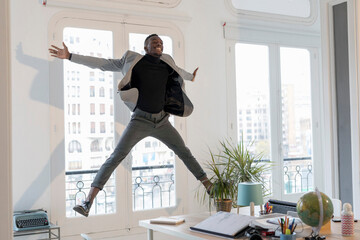 Happy young businessman jumping in the air in his office