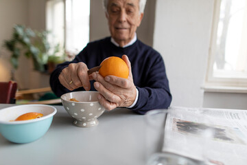 Senior man peeling orange at home