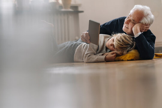 Grandfather and grandson lying on the floor at home using a tablet