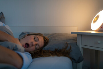 Young woman lying in bed at home at night yawning