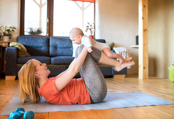 Happy mother lifting up baby at home lying on mat