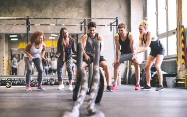 Poster Fitness Group of young fit people cheering at man exercising with ropes in gym