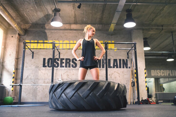 Young woman exercising with tractor tyre in gym