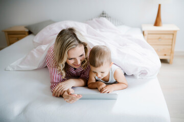 Smiling mother and toddler son lying in bed at home using tablet