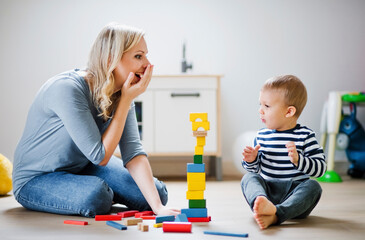 Happy mother and toddler son playing with building blocks at home