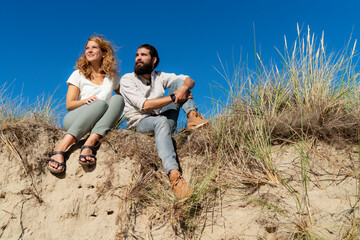 Young couple sitting on a dune in summer, relaxing