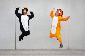 Two women in penguin and lion costume jumping in front of concrete wall