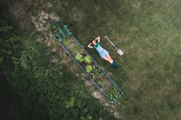Drone shot of woman with hands behind head lying by raised bed on land