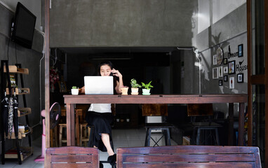Woman sitting at wooden table using laptop and cell phone