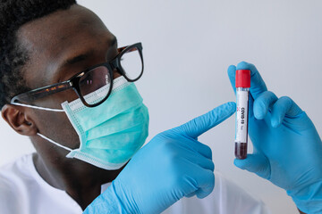 Close-up of afro doctor showing coronavirus blood sample against white background - obrazy, fototapety, plakaty