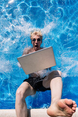 Shocked young man with laptop falling in swimming pool