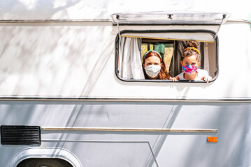 Mother and daughter wearing masks looking through window of motor home