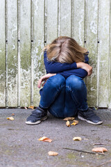 Sad girl crouching in front of wooden wall hiding her face