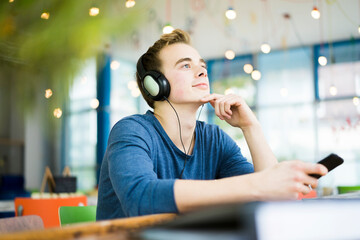 Portrait of young man listening music with headphones in a coffee shop