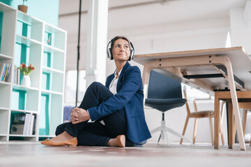 Businesswoman sitting on the floor in a loft listening music with headphones