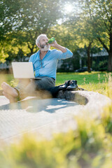 Mature man drinking beer and using laptop in park