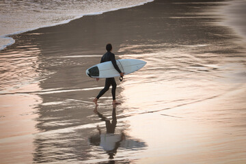Silhouette and reflection of surfer with surfboard on a beach at sunset. Surfer and ocean