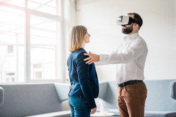 Businessman with VR glasses in office touching businesswoman
