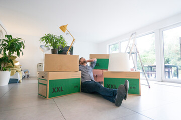 Man sitting on the floor in living room surrounded by cardboard boxes