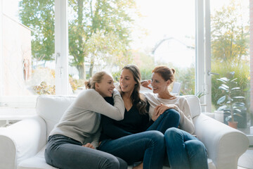 Happy mother with two teenage girls on couch at home