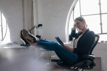 Businesswoman using tablet with feet on desk in office