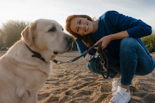 Germany, Hamburg, smiling woman with dog on beach at the Elbe shore
