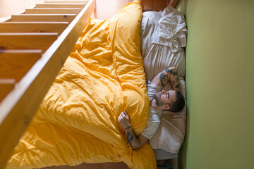 Tattooed man lying in bed, wooden ladder