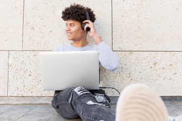 Smiling young man with headphones using laptop in the city