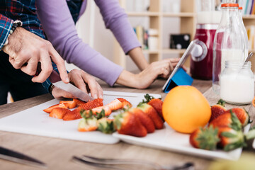 Man chopping strawberries while his girldfriend using tablet, partial view