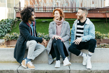 Three happy friends sitting in the city talking