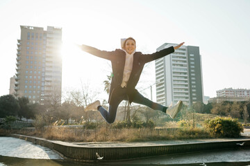 Happy young woman jumping in a park with the city in background