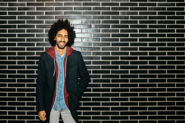 Portrait of a smiling young man standing at a black wall