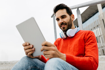 Casual businessman sitting stairs in the city, using his digital tablet and headphones